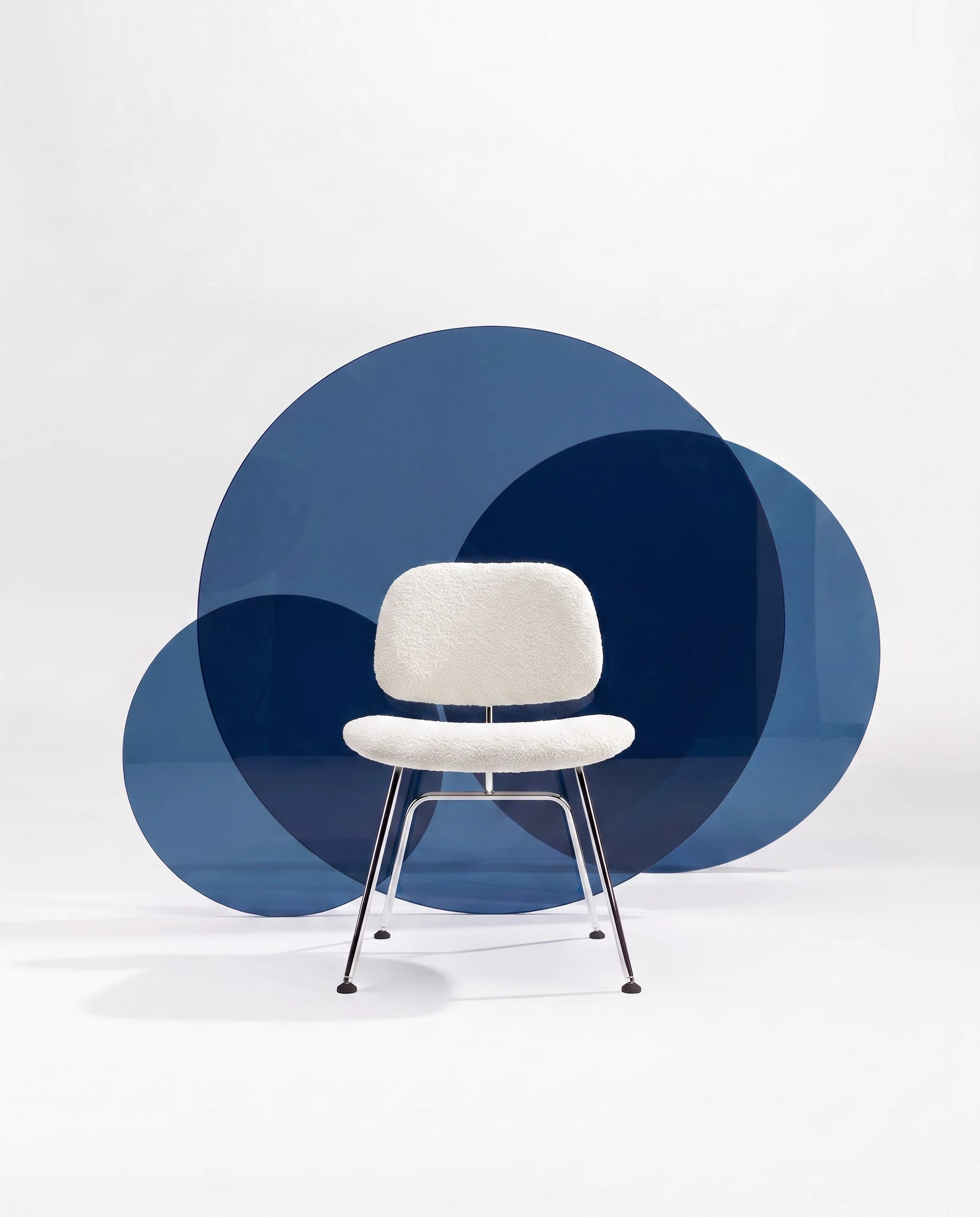 Cadeira Nômia com assento e encosto estofados em off white e base metálica branca diante de círculos translúcidos em azul